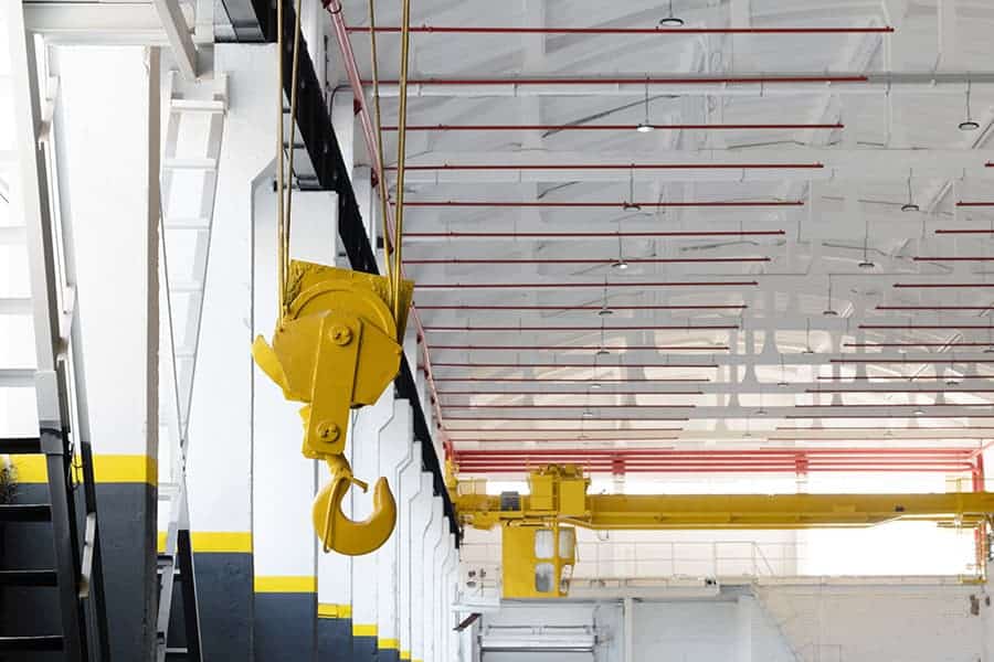 Industrial workshop with an overhead crane fire safety system red pipes. A bright yellow crane hook is suspended from the ceiling. Concept of industry, manufacturing, engineering, interior
