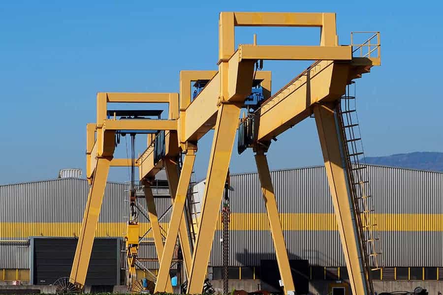 Gantry cranes in front of a gray and yellow building of a manufa